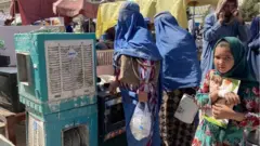 মাজার-ই-শরিফে পুরোনো জিনিসপত্রের এক বাজারে এক আফগান বালিকা। বেঁচে থাকার সংগ্রামে অনেক আফগানকে তাদের সংসারের জিনিসপত্র বিক্রি করে দিতে হচ্ছে।