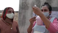 கையில் பச்சிளங் குழந்தையோடு தடுப்பூசிப் பணியில் பெண் சுகாதார அதிகாரி