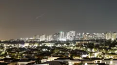 Um rastro de luz ilumina o céu durante um ataque de míssil do Irã em direção a Israel, visto de Ashkelon, Israel, em 7 de junho de 2026.