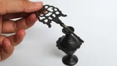 Uma mão feminina segura uma ferramenta antiga para aplicar delineador de kohl e um recipiente de armazenamento antigo