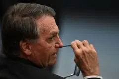 Bolsonaro de costas olhando para algo e segurando óculos
