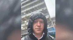 Sol com capuz na chuva em frente a um prédio alto.