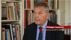 لازيراني في مقابلة عبر بي بي سي يرتدي بدلة رسمية كحلية وقميص أرزق وربطة عنق كحلية عليها نقط بيضاء.