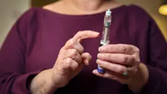 A woman in a burgandy top holds a weight loss injection pen