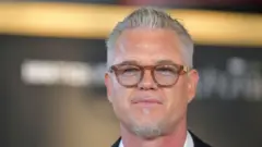 Eric Dane, con cabello gris y gafas de montura marrón