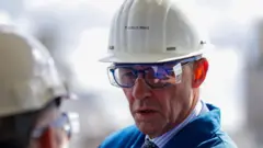 Фридрих Мерц в белой каске с наклейкой со своим именем и защитных очках