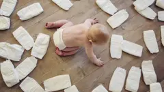 Bebê no chão de madeira, cercado por fraldas descartáveis