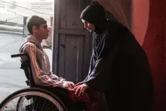 أحد الفتية مبتور الساقين من ضحايا الحرب في غزة يجلس على كرسي متحرك وبمواجهته أمه التي تعتني به بعد أن أصبح معوقا
