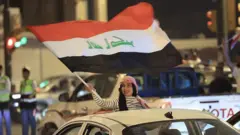 Bir arabadan çıkmış elinde ırak bayrağı olan kutlama yapan bir kadın. 