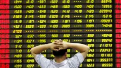 Homem com as mãos na cabeça observando painel com preços de ações