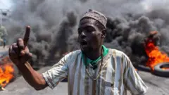 A man stands in front of an enormous plume of smoke as tyres burn