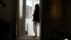 Sara stands at the door with a cup in her hand.