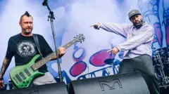 Rivers svira na zelenoj bas gitari, dok Fred Durst ima bradu i nosi ljubičasti džemper.