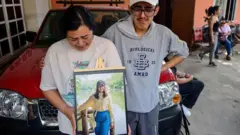 Familiares de América Sánchez sostienen una fotografía enmarcada de la joven cadete en su ciudad natal, Xalapa. En la foto, América Sánchez posa con una blusa amarilla y jeans frente a un lago. Sus familiares lloran.