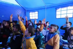 أطفال من تلاميذ المدارس في غزة يجلسون على الأرض في إحدى الخيام لحضور دروس يقدمها معلمون متطوعون ويبدوكثير منهم وقد رفعوا أيديهم طلبا للإجابة عن سؤال