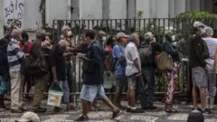 Fila de pessoas com máscara em rua