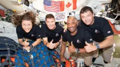 Foto dos quatro tripulantes da Artemis 2, com o polegar para cima, flutuando no interior da espaçonave