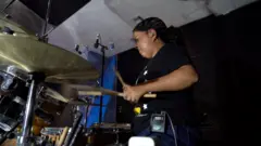 Sara Espinoza, com síndrome de Laron, em frente a uma bateria