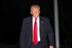 Donald Trump caminhando. Ele usa uma gravata vermelha e terno preto