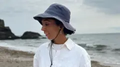 Uma mulher com cabelo castanho encaracolado, usando um boné azul escuro e uma camisa branca