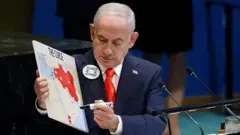 نتانیاهو به نقشه‌ای که در دست دارد نگاه می‌کند؛ بخشی از ترکیه و همسایگان جنوب‌شرقی آن دیده می‌شود. همسایگان با رنگ قرمز علامت‌گذاری شده‌اند. در دست دیگرش یک ماژیک است