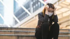 Mulher de máscara sentada de cabeça baixa