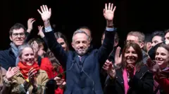 Эмманюэль Грегуар стоит перед микрофоном с поднятыми руками, по его левую руку стоит экс-мэр Парижа Анн Идальго