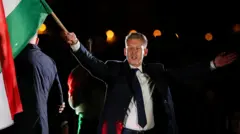 Magyar'ın sağ elinde macaristan bayrağı var, üzerinde koyu renk bir takım elbise ve kravat var. 