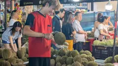 新加坡一位水果攤販正在攤位上開榴槤。