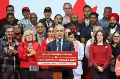 Primeiro-ministro do Canadá Mark Carney em pronunciamento de campanha, tendo atrás dele diversos apoiadores e a bandeira do país