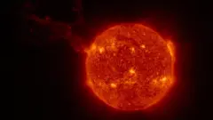 El Sol se ve como una bola roja con puntos brillantes de color amarillo en su superficie; una larga nube se extiende desde la izquierda.