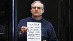 Paul Whelan holds up a sign at the end of his trial - "Sham trial! Meatball surgery! No human rights! Paul's life matters! Decisive action from potus and PMs needed! Happy Birthday Flora!"