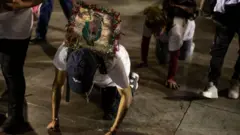 Devotos, agachados a gatas sobre el piso, con la imagen de la virgen a sus espaldas