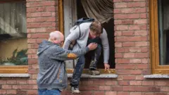 Schuld: man helping woman from flood-hit building, 15 Jul 21