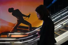 Una mujer sube por una escalera mecánica pasando junto a un cartel de la película Bohemian Rhapsody en un cine de Pekín el 27 de marzo de 2019.