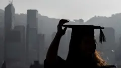 一名大學畢業生穿著畢業袍在香港維多利亞港旁拍照。