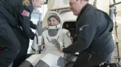 Suni sorrindo ao deixar cápsula, auxiliada por outras pessoas