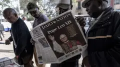 أربعة رجال يقفون عند كشك لبيع الصحف في أحد شوارع نيروبي، يتصفحون الصحف التي تحمل صورة البابا ليو الرابع عشر على صفحتها الأولى.