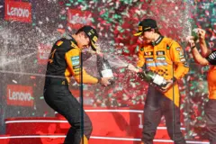 Dois pilotos no pódio estourando champanhe e comemorando