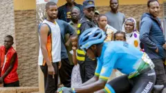 Umunyarwanda w'umugabo urimo gusiganwa ku igare, iruhande rwe ku muhanda hari abantu baje kureba isiganwa, muri Gashyantare (2) mu 2024