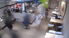 A group of teenagers, blurred, run amok in a shop as they carry out antisocial behaviour, as seen from a CCTV camera at a high angle.