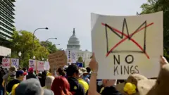 Manifestantes marcham em frente ao Capitólio em Washington, D.C. Uma pessoa carrega uma placa que diz "Sem Reis".