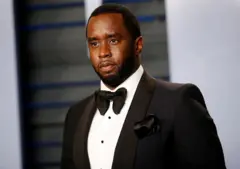 Diddy posando com roupa de gala, em pé em evento; ele tem olhar sério
