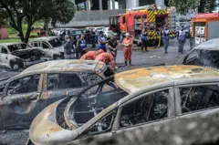 Bombeiros e policiais trabalham ao lado de veículos incendiados no local da queda de helicópteros no bairro do Recreio dos Bandeirantes