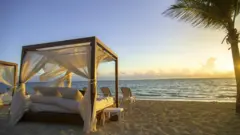 A four poster bed on a tropical beach, at sunset