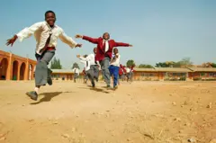 Awọn ọmọde to wọ aṣọ ile-ẹkọ wọn, to si n sare pẹlu idunnu ninu ọgba ile-ẹkọ