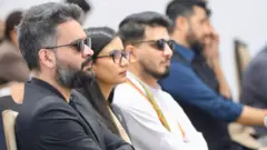 कालो कोट र कालो चस्मा लगाएका प्रधानमन्त्री वालेन्द्र शाहसँगै कानुन मन्त्री सोबिता गौतम र पूर्वाधार विकास मन्त्री सुनिल लम्साल। पृष्ठभूमिमा रास्वपाका अध्यक्ष रवि लामिछाने देखिन्छन्