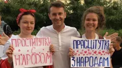 ведущий на протесте с плакатом "проститутки с народом"