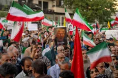 Vários iranianos protestando nas ruas com a bandeira do país e uma imagem de Trump