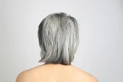 Fotografia de um homem com cabelos grisalhos, visto de costas, contra um fundo branco neutro.